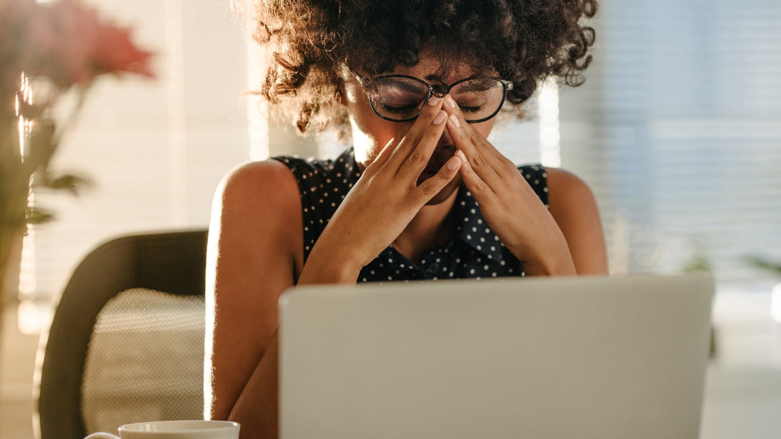 Tired stressed woman sitting at computer showing how stress and fatigue contribute to premature skin aging and dull skin