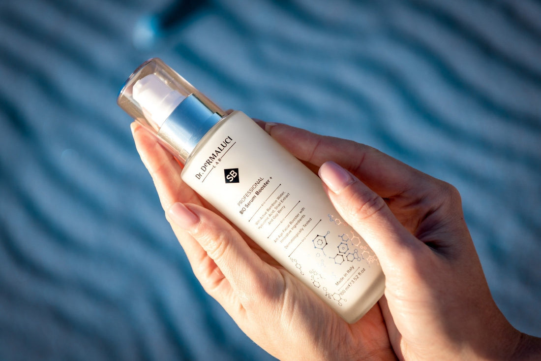 Hand holding Dr. Dermaluci Lab BIO Serum Booster bottle on rippled blue background, Made in Italy