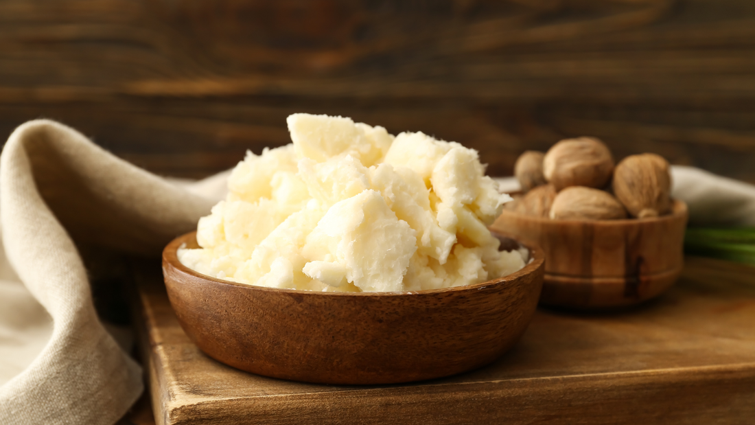 Creamy white body butter in a wooden bowl on dark wood, with whole nutmeg seeds in a smaller bowl behind