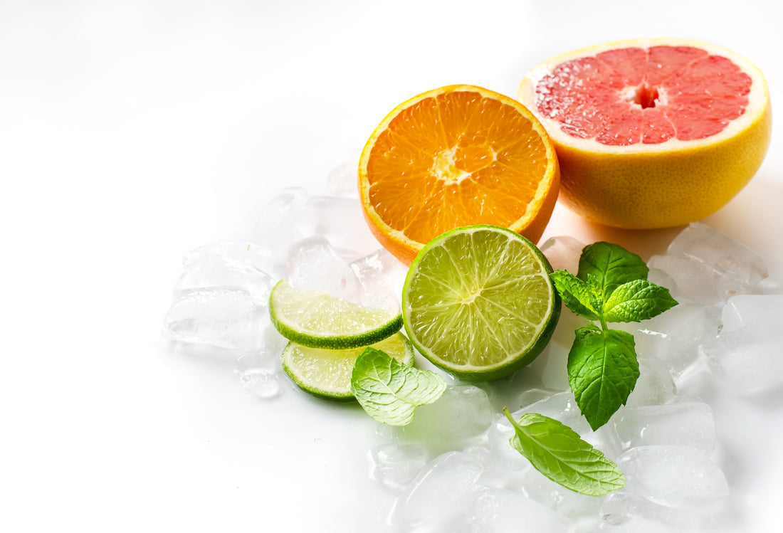 Fresh orange, grapefruit and lime halves with mint sprigs on crushed ice against a white background