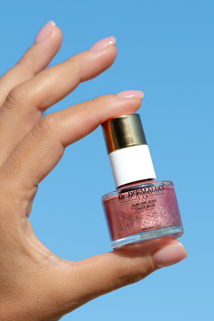 Hand holding a bottle of Dr. Dermaluci Lab Rose Blush against a blue background